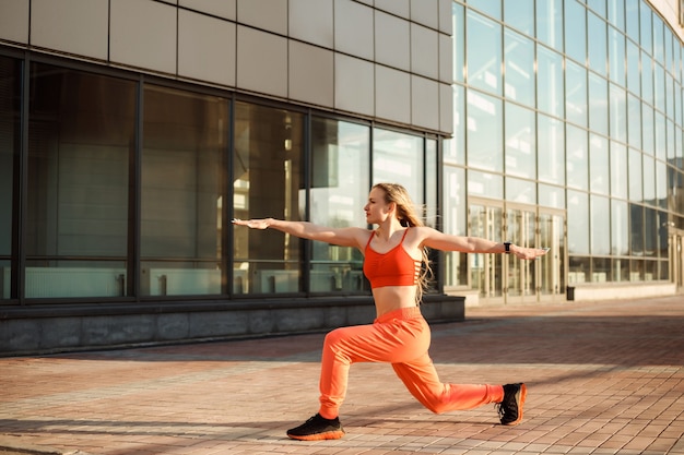 Attraktive Frau praktiziert Yoga und steht in der Pose des Kriegers zwei vor dem städtischen Gebäude.