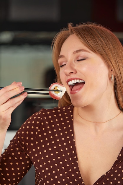 Attraktive Frau ruht sich zu Hause mit Sushi aus, isst Sushi mit Stäbchen, schließt Essen ab und nimmt es mit.