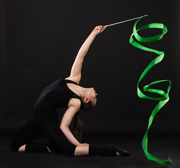 Attraktive Frau tanzt mit grünem Band vor dunklem Hintergrund