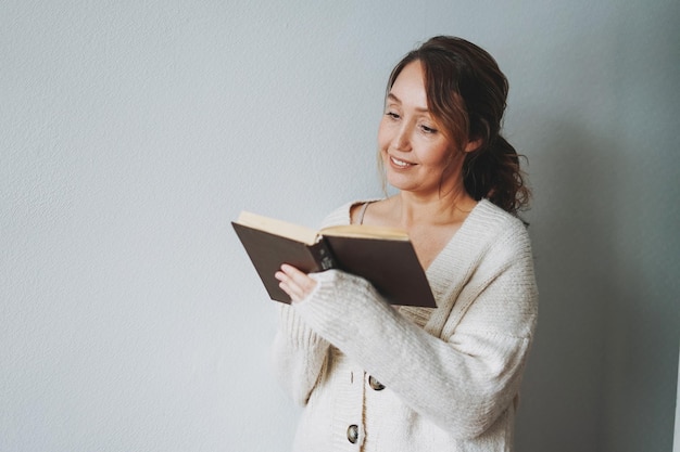 Attraktive freundliche lächelnde brünette Frau mittleren Alters Lesebuch zu Hause gemütliche Stimmung Wintersaison