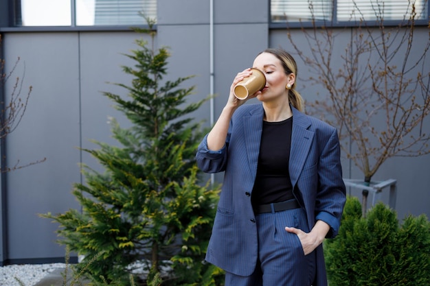 Attraktive Geschäftsfrau in formeller Kleidung trinkt Kaffee, während sie während einer Pause im Freien steht