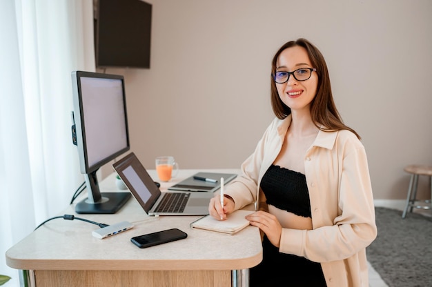 Attraktive Geschäftsfrau in Freizeitkleidung, die zu Hause am Laptop arbeitet und sich Notizen macht Junge glückliche Studentin, die an der Online-Universität studiert