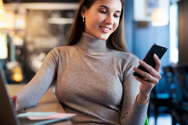 Attraktive Geschäftsfrau sitzt am Tisch vor dem Laptop und spricht auf dem Handy, verhandelt am Telefon.