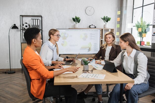 Attraktive Geschäftsfrauen sitzen im modernen Büro zusammen und arbeiten an Tablets und Laptops