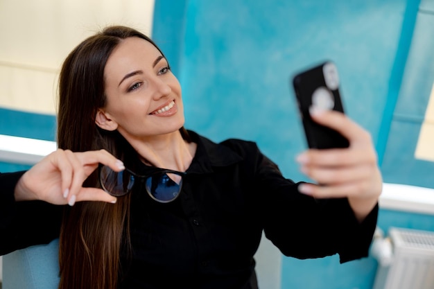 Attraktive glückliche Frau macht Selfie mit Brille Hübsche junge Frau, die die Kamera ihres Telefons betrachtet und lächelt