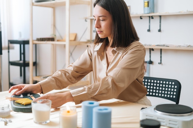 Attraktive Handwerkerin bereitet den Arbeitsplatz am Tisch vor, um in der Werkstatt handgefertigte Kerzen herzustellen. Verfahren zur Herstellung von handgefertigten natürlichen Kerzen zu Hause.