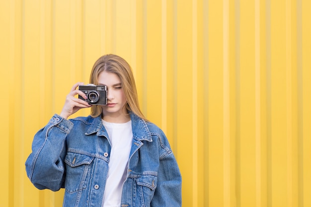Attraktive Hipistin fotografiert auf einer Filmkamera an einer gelben Wand.