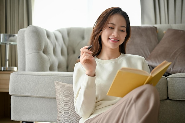 Attraktive junge asiatische Frau sitzt im minimalistischen Wohnzimmer und liest gerne ein Buch