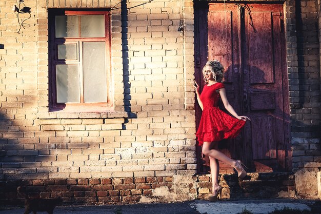 Attraktive junge Blondine im roten Kleid, die auf dem Hintergrund eines alten Backsteingebäudes aufwirft.