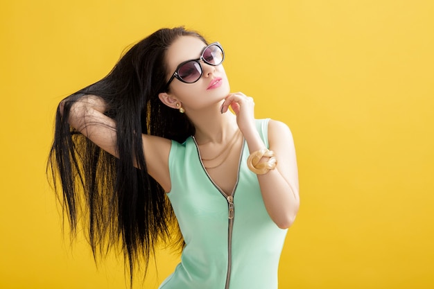 Attraktive junge Brunettefrau in einem grünen Badeanzug auf einem Gelb. Sommer sexy Frau in einem türkisfarbenen Body und Sonnenbrille