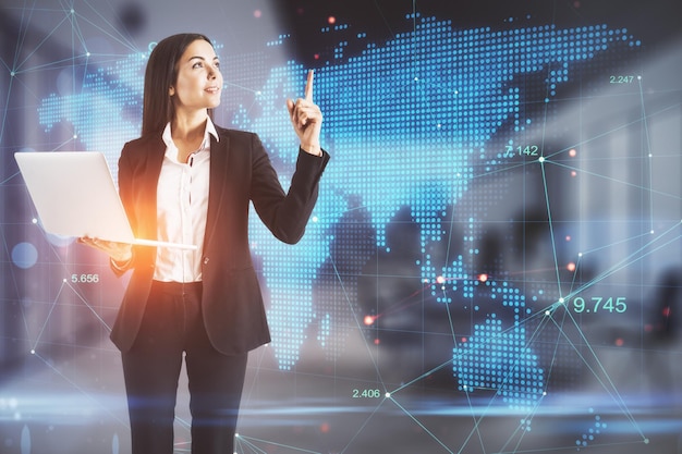 Attraktive junge europäische Geschäftsfrau mit futuristischer Touchscreen-Karte und Laptop im verschwommenen Bürointerieur Doppelbelichtung