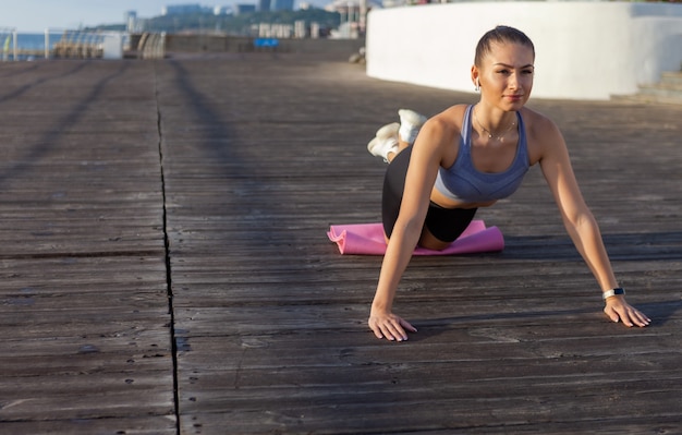 Attraktive junge Fitnessfrau, die bei Sonnenaufgang Liegestütze am Strand praktiziert