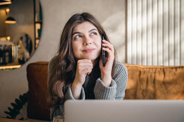 Attraktive junge Frau, die am Telefon spricht und an einem Laptop arbeitet