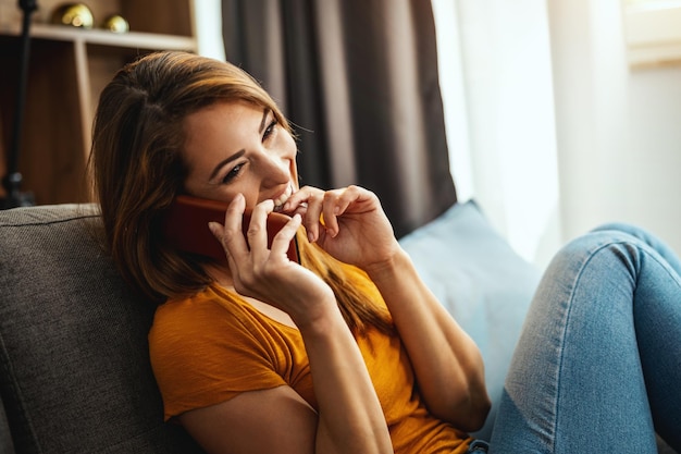 Attraktive junge Frau, die auf dem Sofa sitzt und zu Hause Smartphone benutzt.