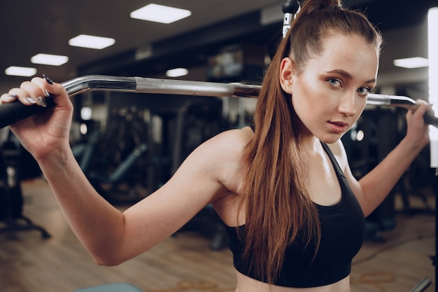 Attraktive junge Frau, die Übungen für die Muskeln der Arme und zurück in einem Fitnessstudio macht