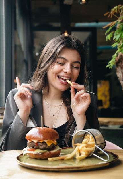 Attraktive junge Frau, die in einem Restaurant Pommes Frites und einen Burger isst