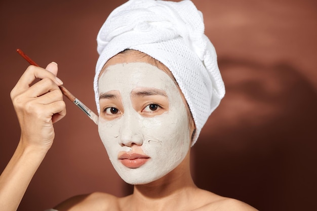 Attraktive junge Frau, die kosmetische Maske auf ihrem Gesicht anwendet.