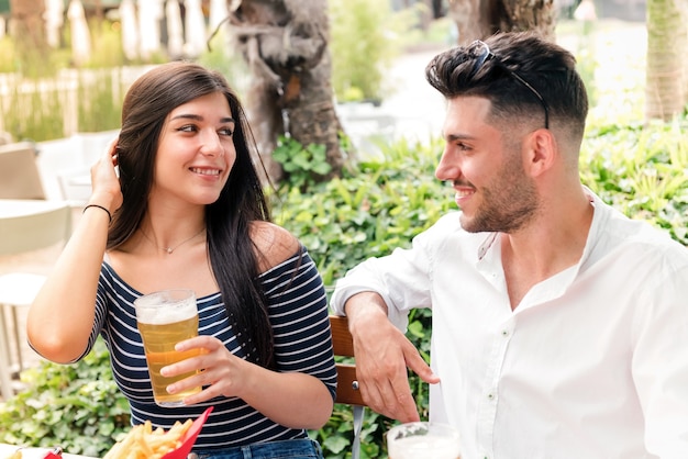 Attraktive junge Frau, die mit einem Mann bei Bier in einem Restaurant oder Pub im Freien flirtet, während sie ein romantisches Date genießen und sich gegenseitig in die Augen lächeln
