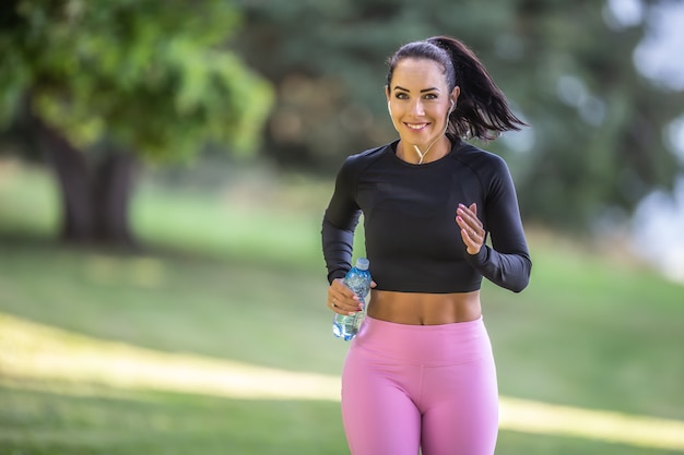 Attraktive junge Frau, die mit einer Flasche Wasser im Park läuft.