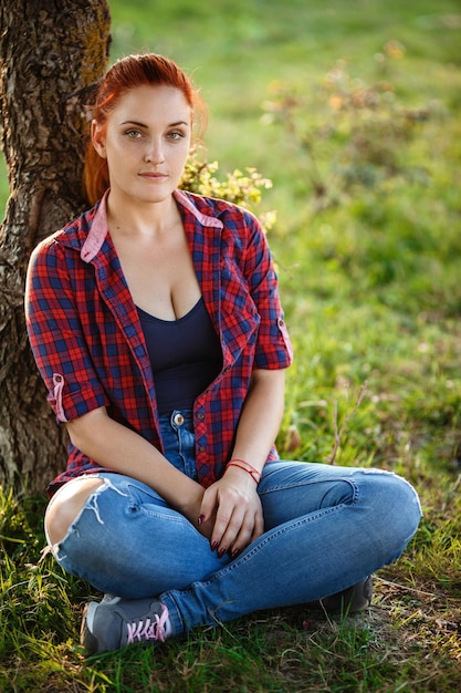 Attraktive junge Frau genießt ihre Zeit draußen im Park mit Sonnenuntergang im Hintergrund Frau in kariertem Hemd und Jeans gekleidet