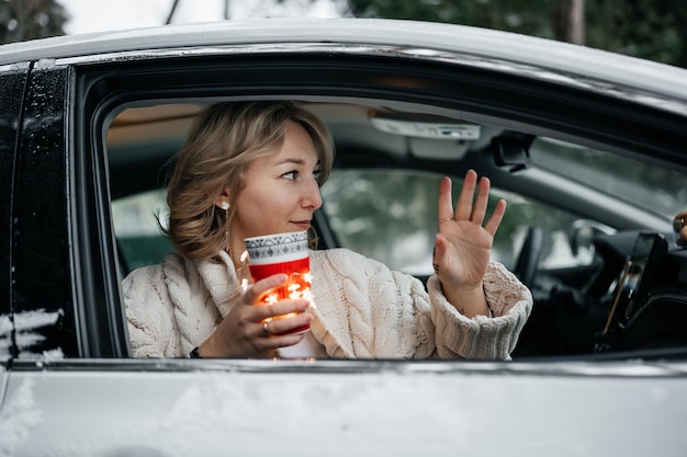 Attraktive junge Frau hält eine Tasse Tee und schaut aus dem Autofenster