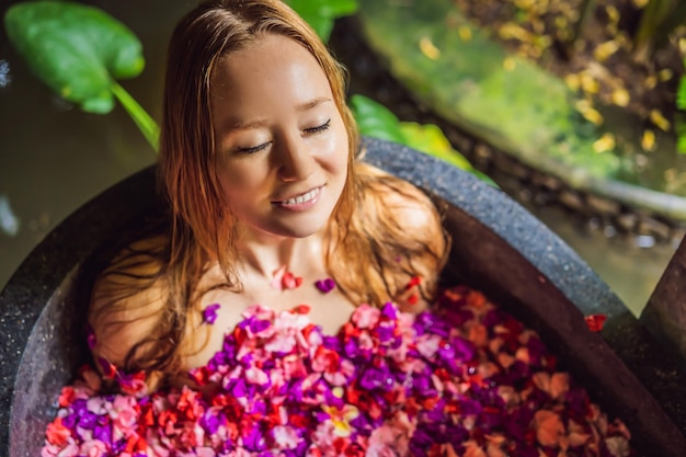 Attraktive junge Frau im Bad mit Blütenblättern tropischer Blumen und Aromaöl-Spa-Behandlungen für