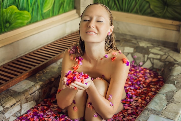 Foto attraktive junge frau im bad mit blütenblättern tropischer blumen und aromaölen. spa-behandlungen zur hautverjüngung. anziehende frau im spa-salon. mädchen, das sich im whirlpool mit blütenblättern entspannt. luxus sp