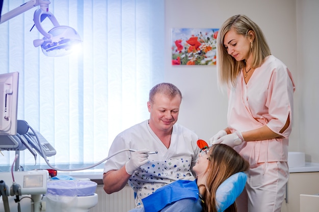 Attraktive junge Frau in der Stomatologieklinik mit männlichem Zahnarzt und seinem Assistenten.