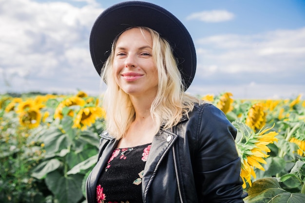 Attraktive junge Frau in schwarzer Lederjacke und Hut posiert auf einem Sonnenblumenfeld