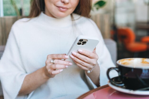 Attraktive junge Frau in weißem Freizeitkleid mit einer Tasse Kaffee mit Handy im Café