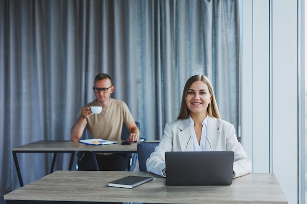 Attraktive junge Frau mit Brille sitzt an einem Tisch mit Laptop in einem Coworking Space und bespricht mit einem Kollegen einen Projektplan Workflow im Büro