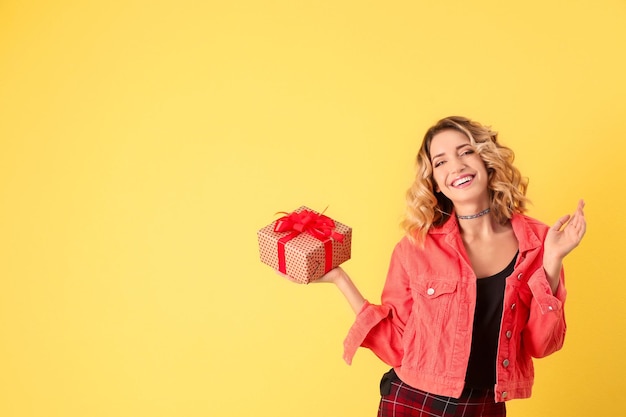 Attraktive junge Frau mit Geschenkbox auf farbigem Hintergrund