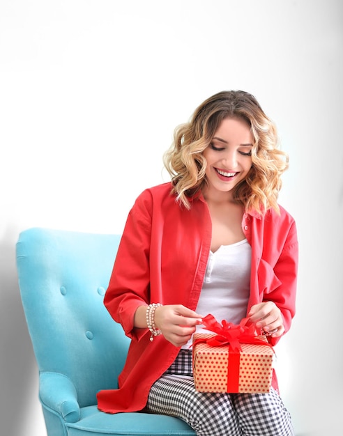 Attraktive junge Frau mit Geschenkbox, die im Sessel neben der Farbwand sitzt
