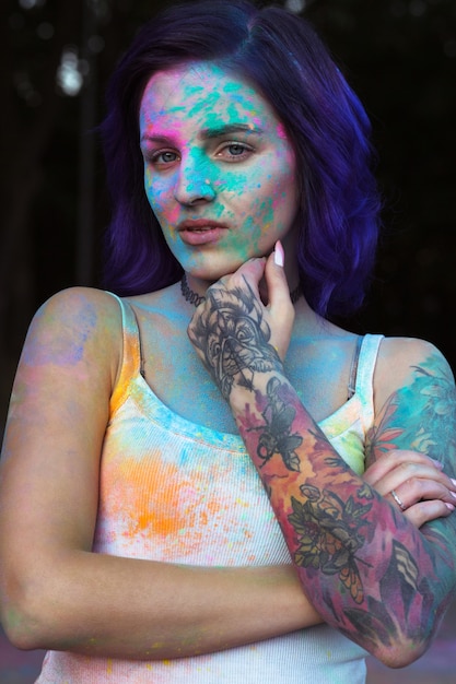 Attraktive junge Frau mit lila Haaren und Tattoo am Arm, bedeckt mit buntem Holi-Pulver