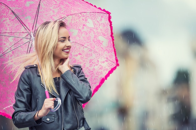 Attraktive junge Frau mit rosa Regenschirm im Regen und starkem Wind