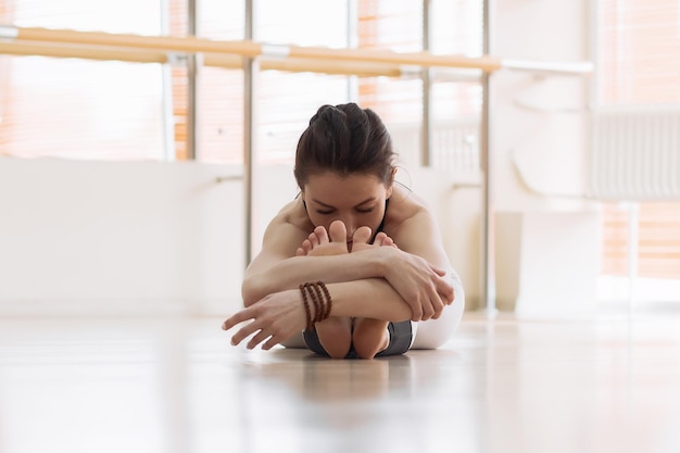 Attraktive junge Frau sitzt auf Studioboden und beugt sich leicht nach vorne, während sie Yoga praktiziert