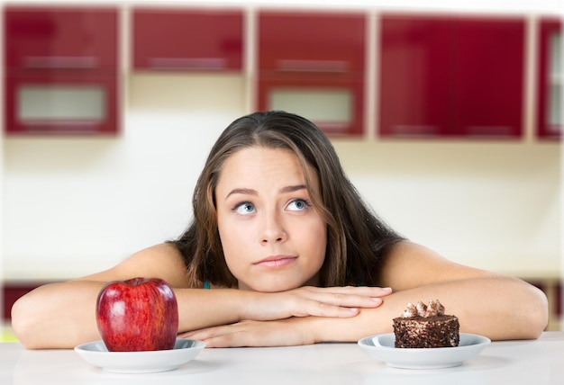 Attraktive junge Frau trifft ihre Wahl zwischen Apfel und Kuchen, gesundes Lifestyle-Konzept