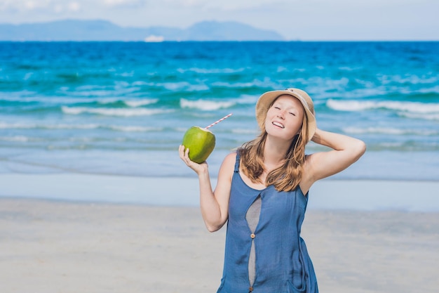 Attraktive junge Frau trinkt Kokoswasser am Strand