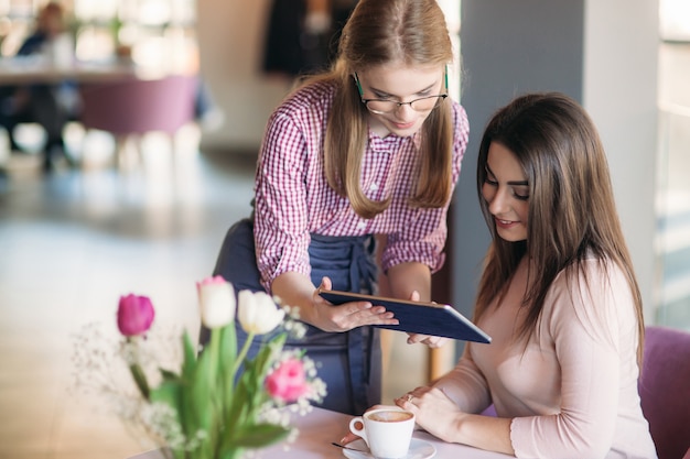 Attraktive junge Kellnerin mit einem Tablet-Computer, um eine Bestellung von einem Kunden in einem Café entgegenzunehmen.