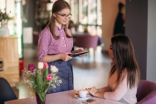 Attraktive junge Kellnerin mit einem Tablet-Computer, um eine Bestellung von einem Kunden in einem Café entgegenzunehmen.