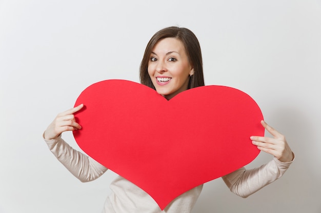 Attraktive junge lächelnde Frau, die großes rotes Herz in den Händen lokalisiert auf weißem Hintergrund hält. Kopieren Sie Platz für Werbung. Mit Platz für Text. Valentinstag- oder Internationaler Frauentag-Konzept.