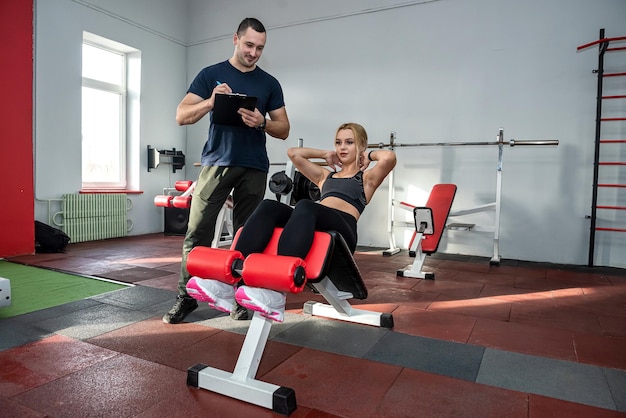 Attraktive junge männliche Trainer und weibliche Kunden, die im Fitnessstudio trainieren, gesunder Lebensstil