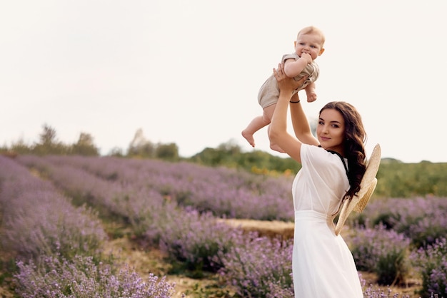 Attraktive junge Mutter, die mit ihrem Baby auf einem Lavendelgebiet spielt