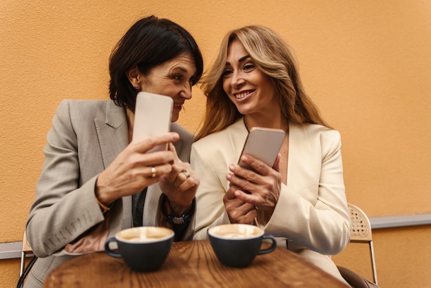 Attraktive kaukasische erwachsene Frauen trinken Kaffee im Café und schauen sich Telefone auf der Straße an Happy Weekend Konzept