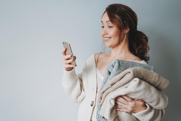 Attraktive lächelnde brünette Frau mittleren Alters mit Strickpullovern mit Handy zu Hause gemütliche Stimmung