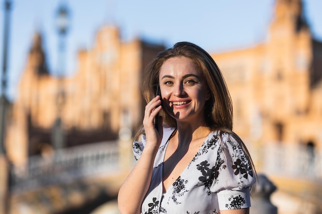 Attraktive lächelnde Frau, die an ihrem Telefon spricht, während sie in die Kamera schaut