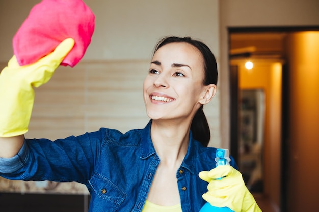 Attraktive lächelnde Frau, die das Fenster mit Spray und Lappen wäscht