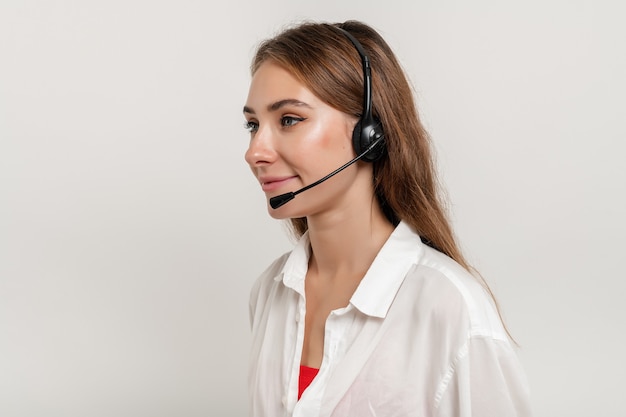 Attraktive lächelnde Frau, die mit Headset als Tech-Support-Dispatcher arbeitet, isoliert über Weiß