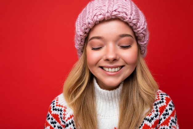 Attraktive lächelnde glückliche junge blonde Frau, die isoliert über bunter Hintergrundwand steht und das alltägliche stilvolle Outfit trägt, das Gesichtsgefühle zeigt.