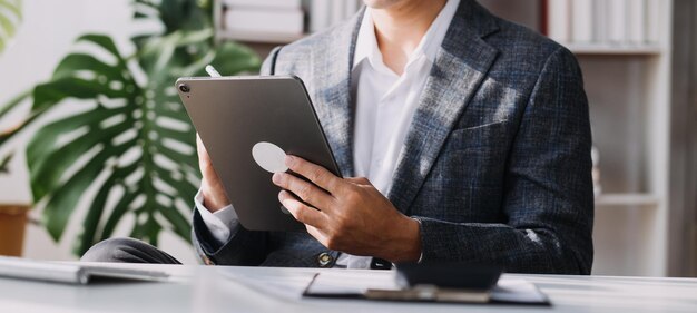 Attraktive lächelnde junge asiatische Geschäftsfrau, die zu Hause im Büro arbeitet Asiatische Frau, die an einem Laptop-Computer mit Tablet arbeitet